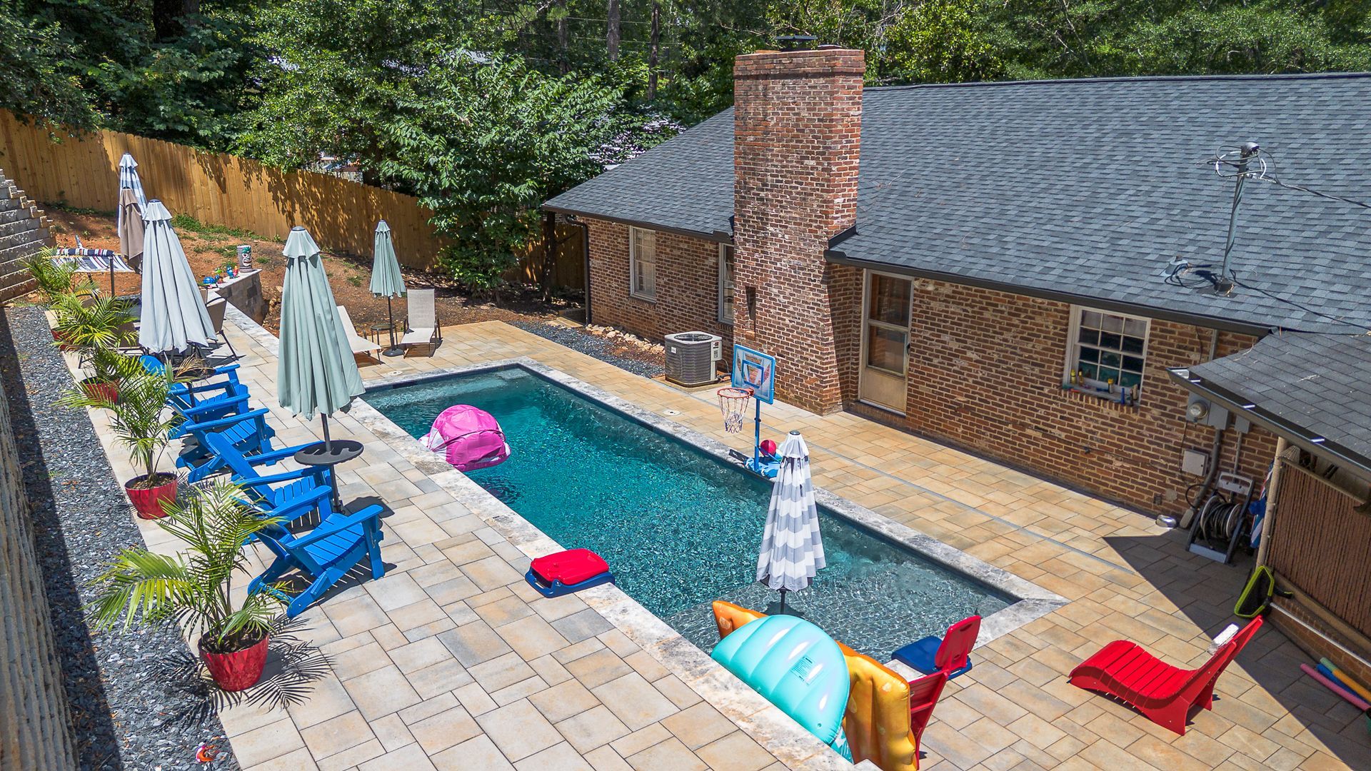 Backyard pool with blue chairs, umbrellas, inflatables, and a brick chimney.