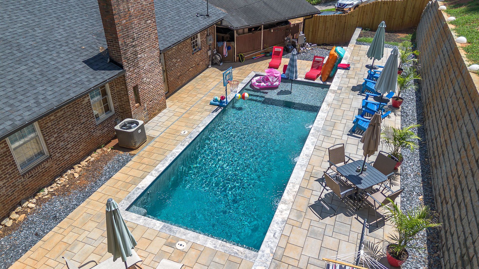 Backyard pool with brick house, kids' toys, and outdoor seating.