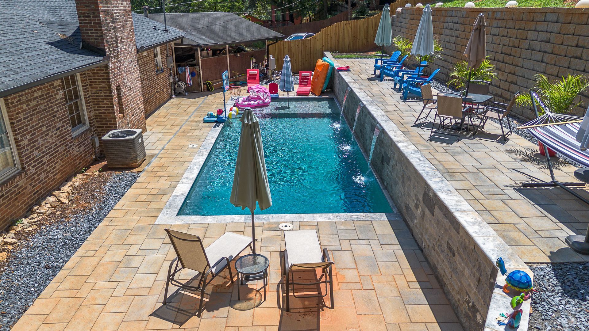 Backyard pool with lounge chairs, umbrellas, and a brick wall.