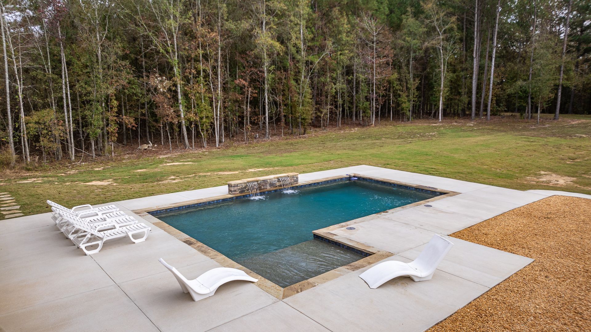 There is a large swimming pool in the middle of a lush green field.