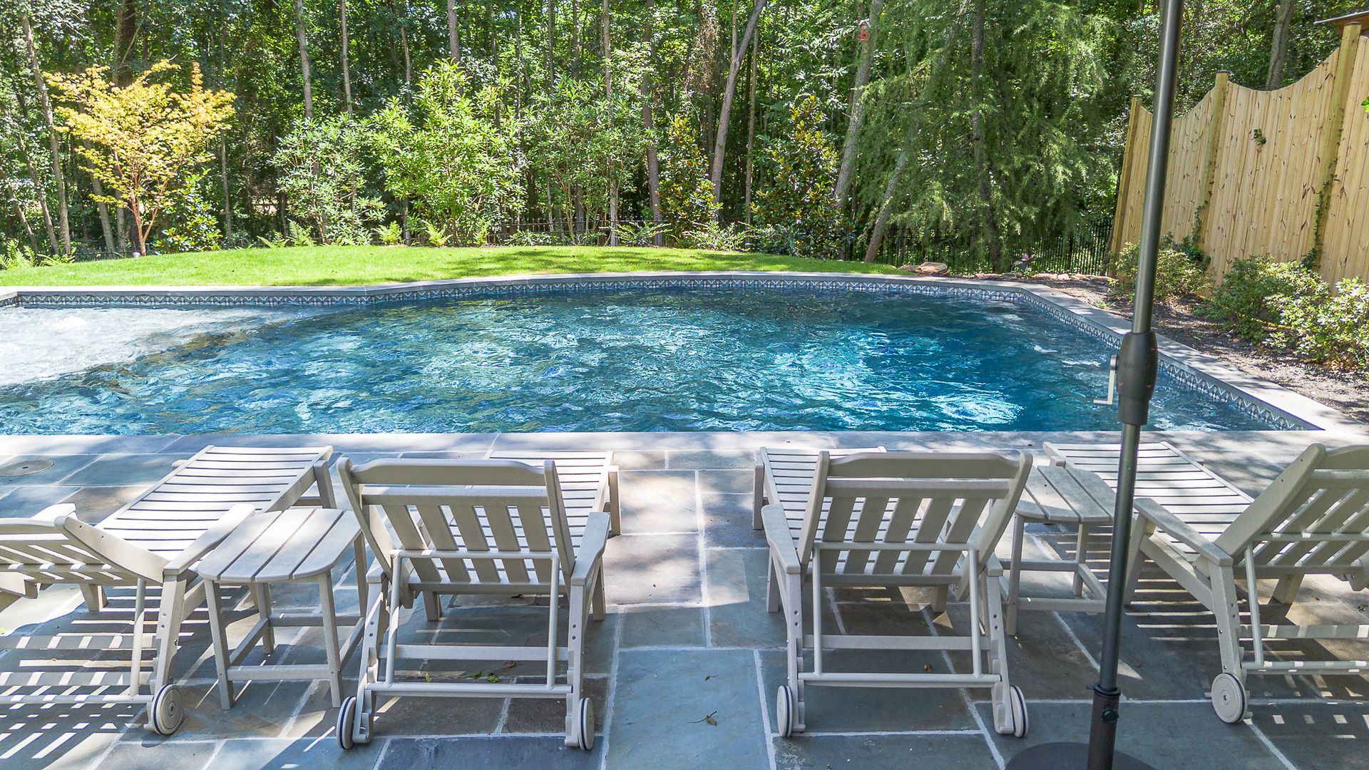 Swimming pool with lounge chairs, surrounded by greenery.