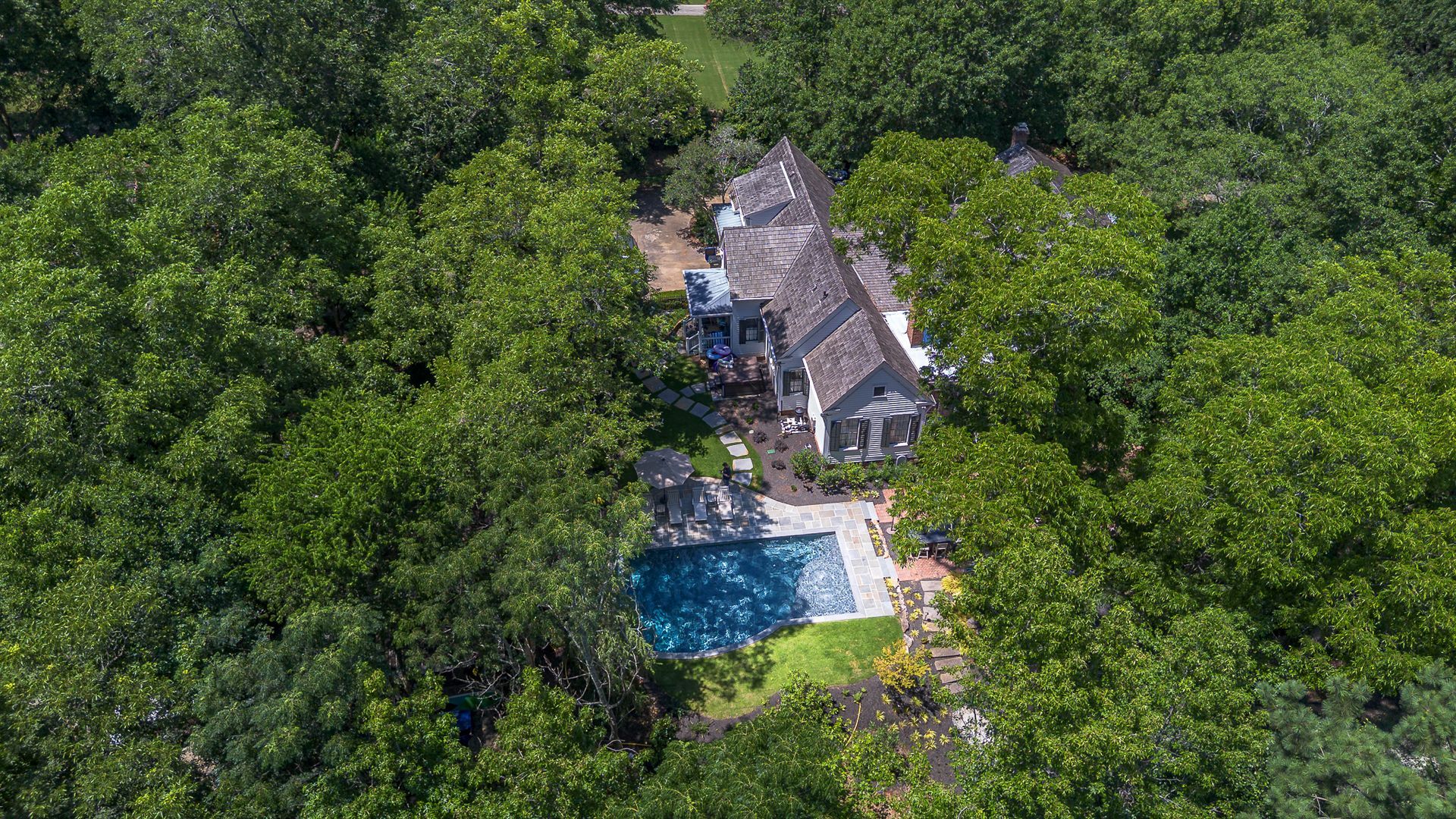 Aerial view of a house with a pool surrounded by lush green trees.