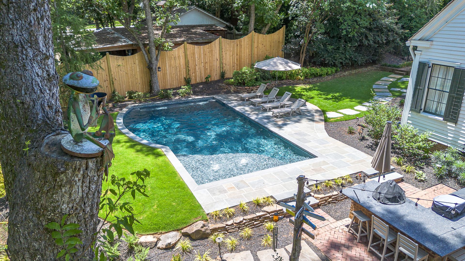 Backyard with pool, lounge chairs, and a white house.  Green grass and a bamboo fence surround the pool.