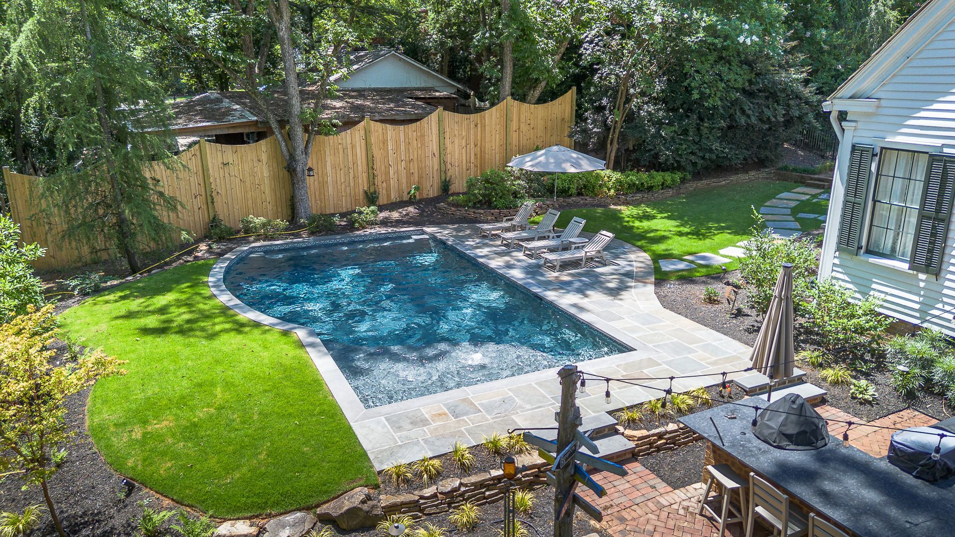 Backyard with a pool, green grass, bamboo fence, and a white house.