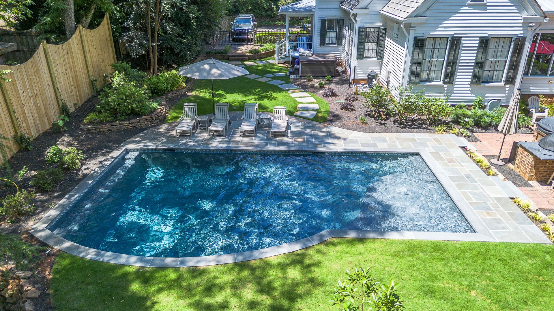 Backyard with a pool, lounge chairs, and a white house.