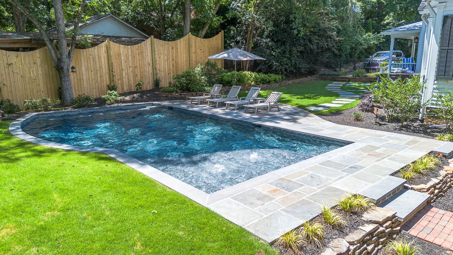 Swimming pool in backyard with lawn and bamboo fence; lounge chairs and steps.