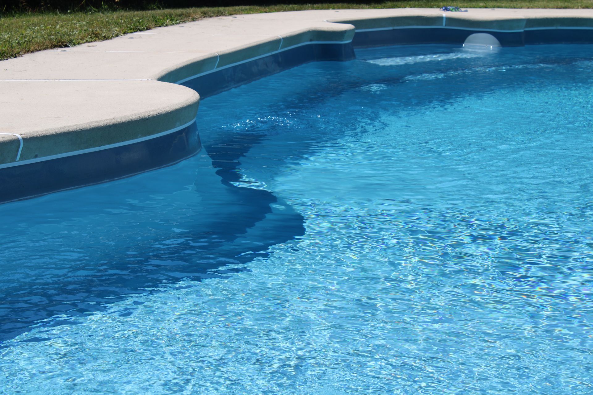 Blue swimming pool with light-colored concrete coping. Clear, rippling water.