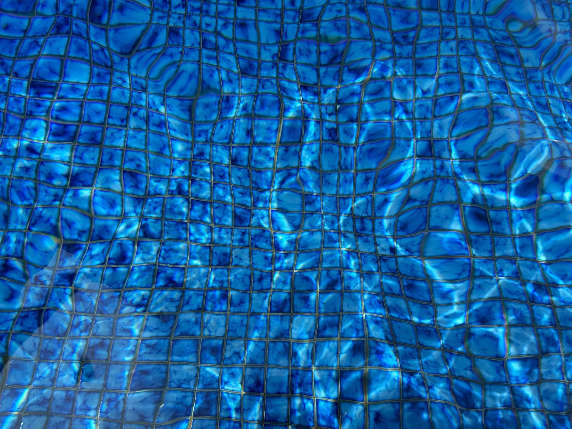 Blue swimming pool water reflecting light, showing square tile pattern.