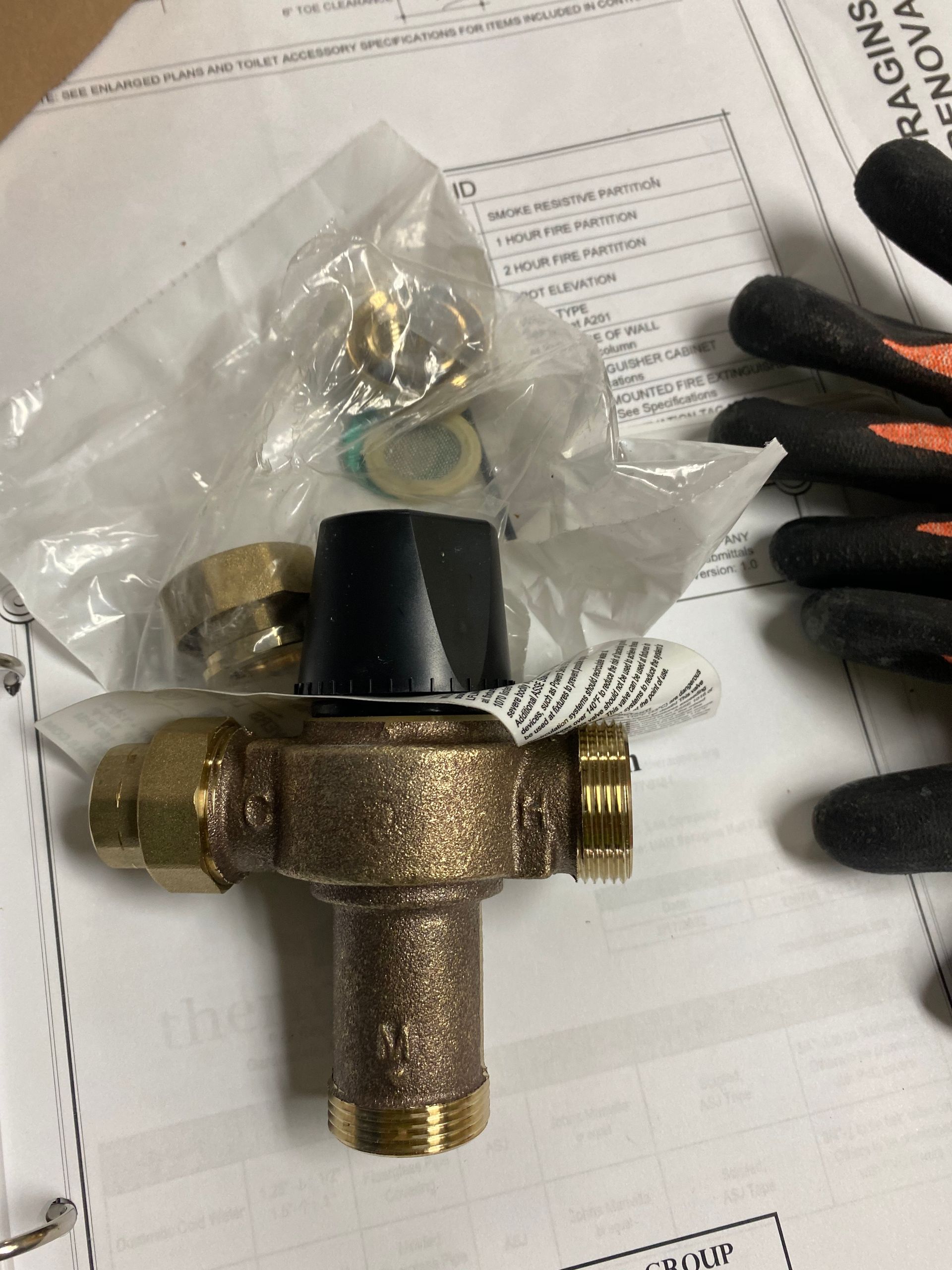 A brass valve is sitting on top of a piece of paper next to a pair of gloves.