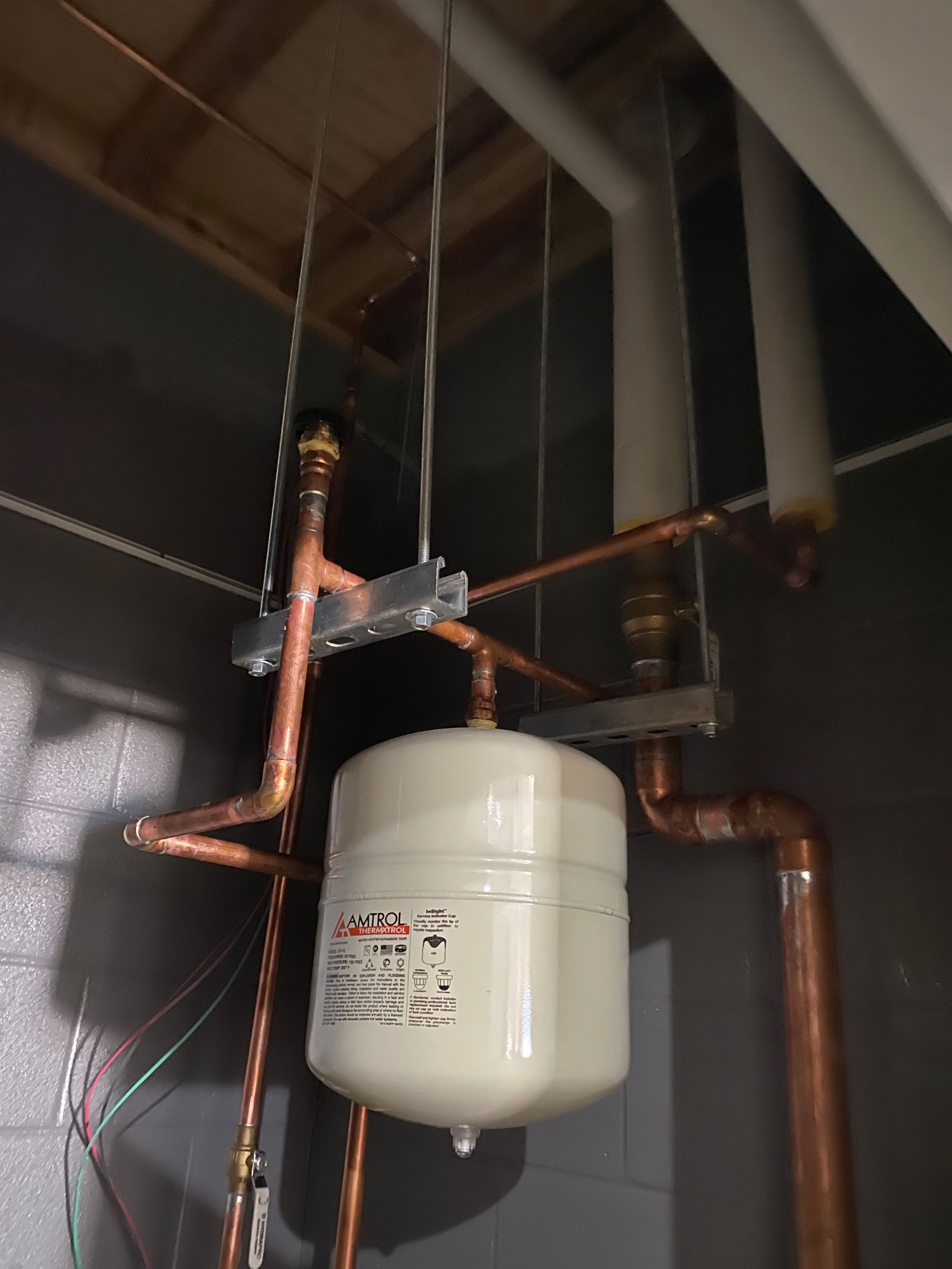 A white tank is hanging from the ceiling next to copper pipes
