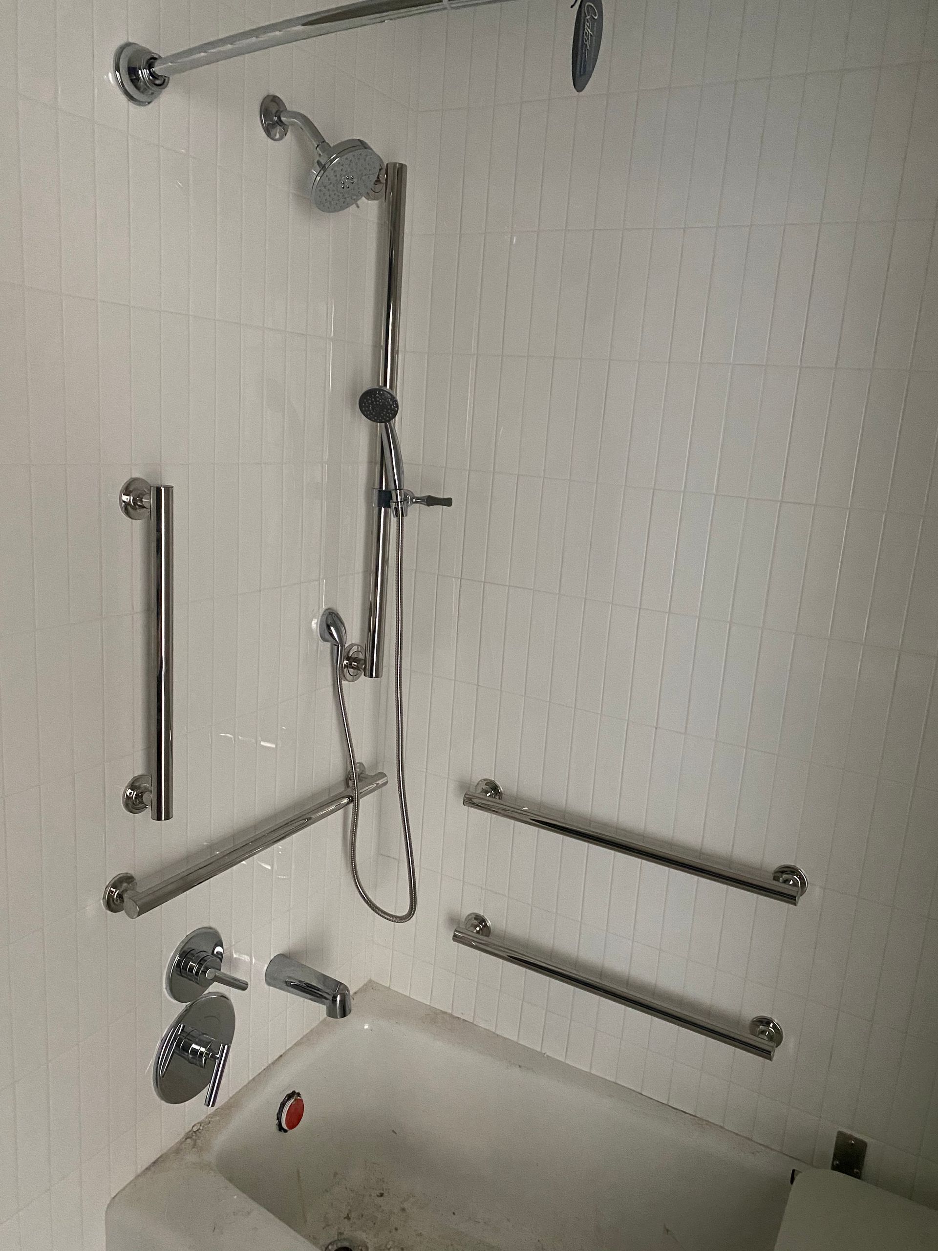 A bathroom with a tub , shower , and handrails.
