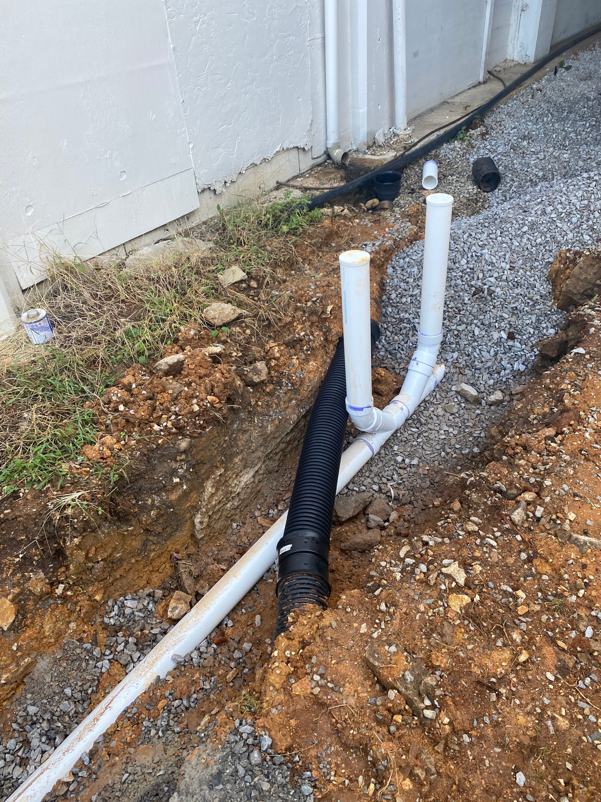 A drain pipe is being installed in the dirt next to a house.