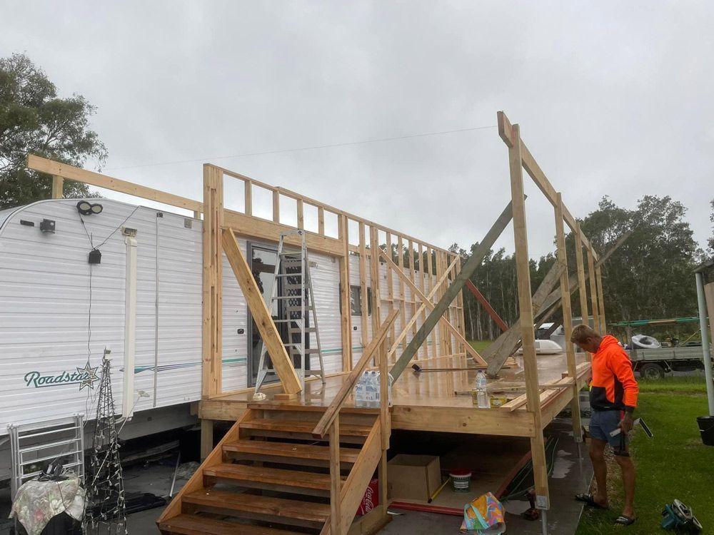 A Man Is Working on A Wooden Deck in Front of A Trailer — J’s Concreting & Carpentry in Kew, NSW