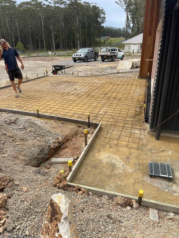 A Man Is Walking on A Dirt Road in Front of A Building Under Construction — J’s Concreting & Carpentry in Kendall, NSW