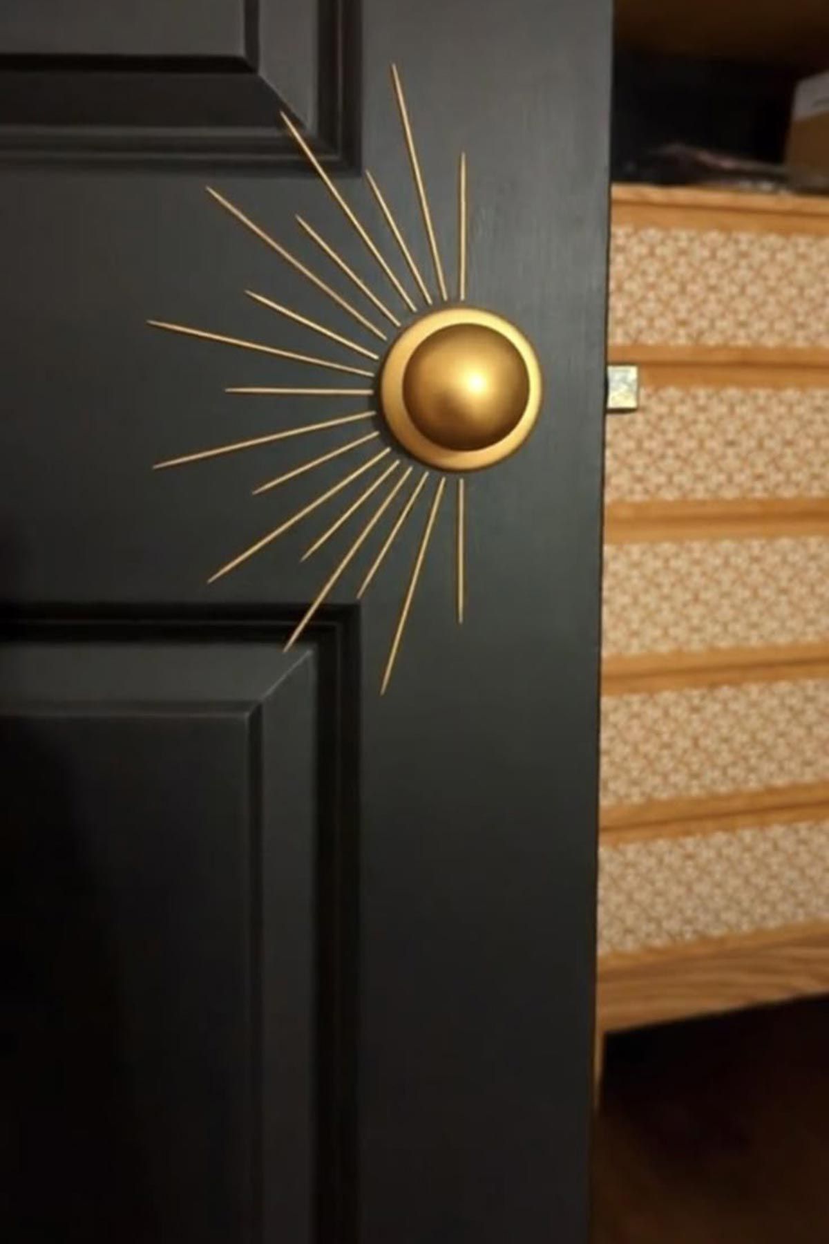 A black door with a gold knob that looks like a sun