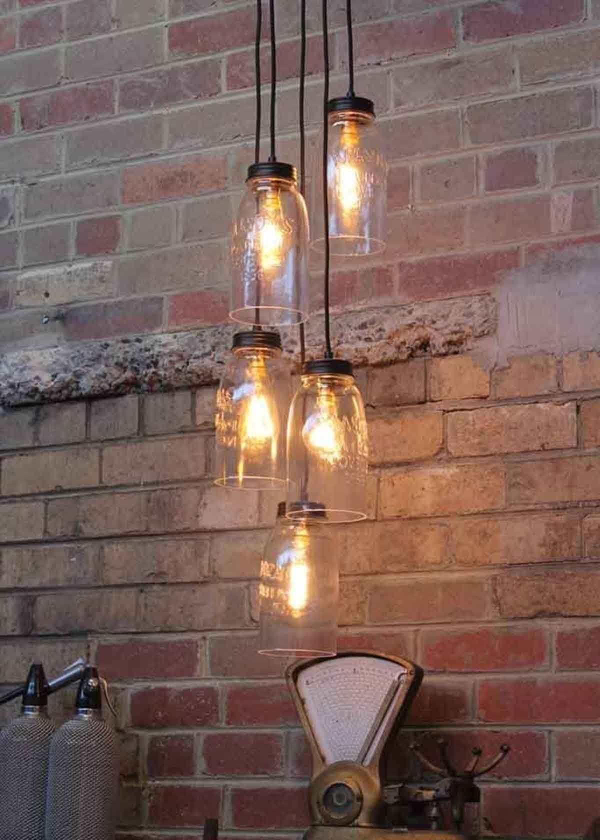 A row of mason jar lights hanging from the ceiling in front of a brick wall.