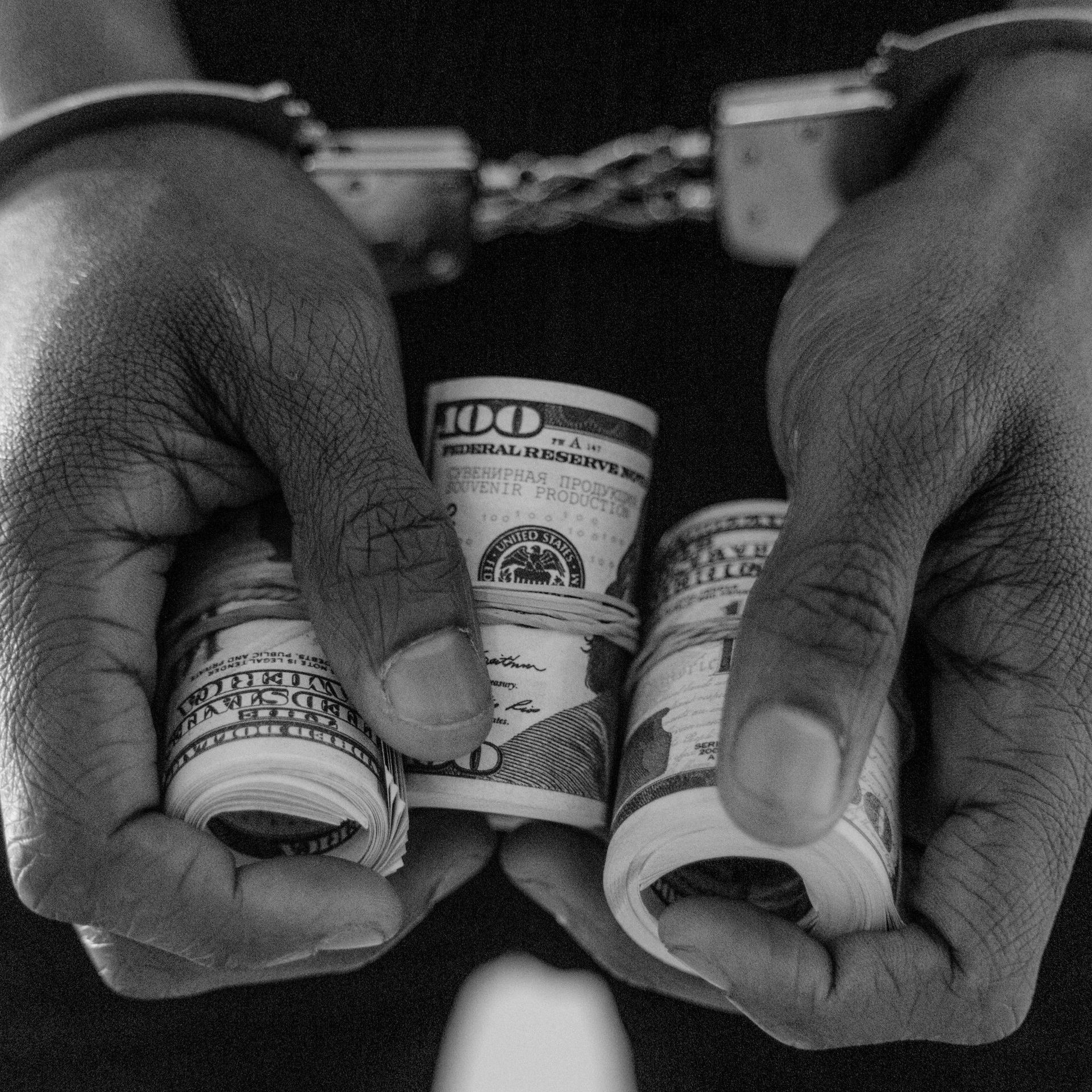 A man in handcuffs is holding two rolls of money in his hands.