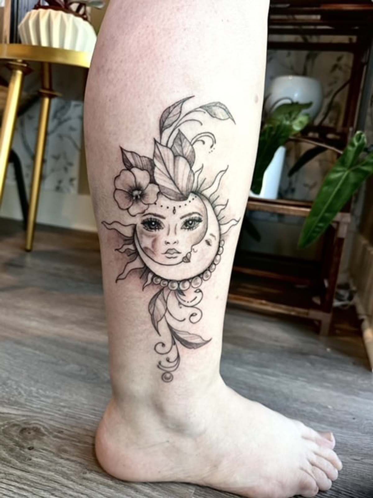 A woman has a tattoo of a sun and a crescent moon on her leg.