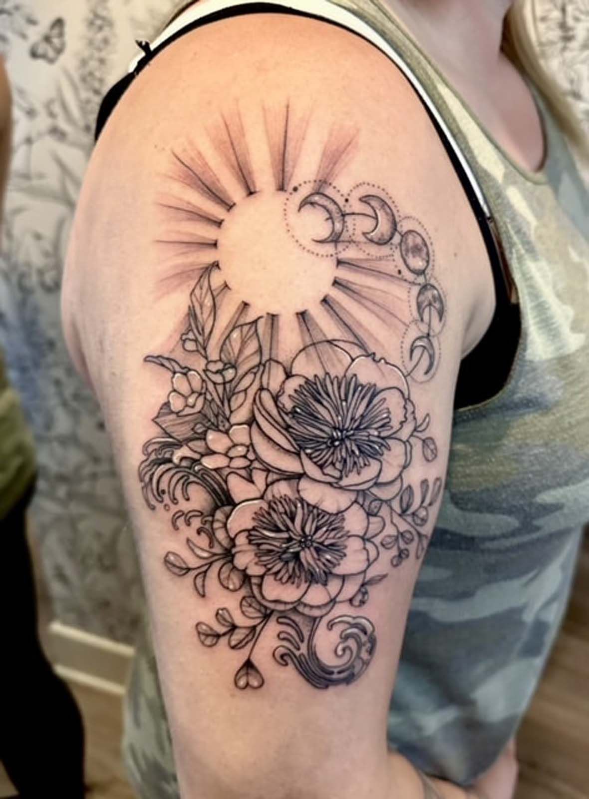 A woman has a tattoo of a sun and flowers on her arm