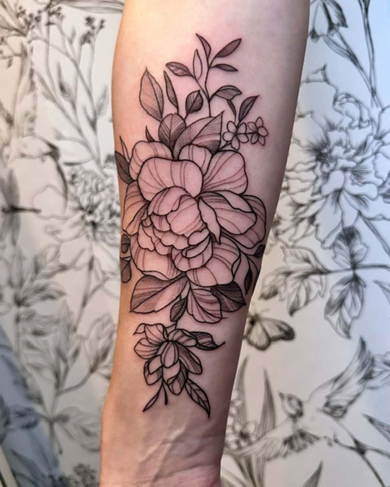 A woman has a tattoo of flowers and leaves on her forearm.