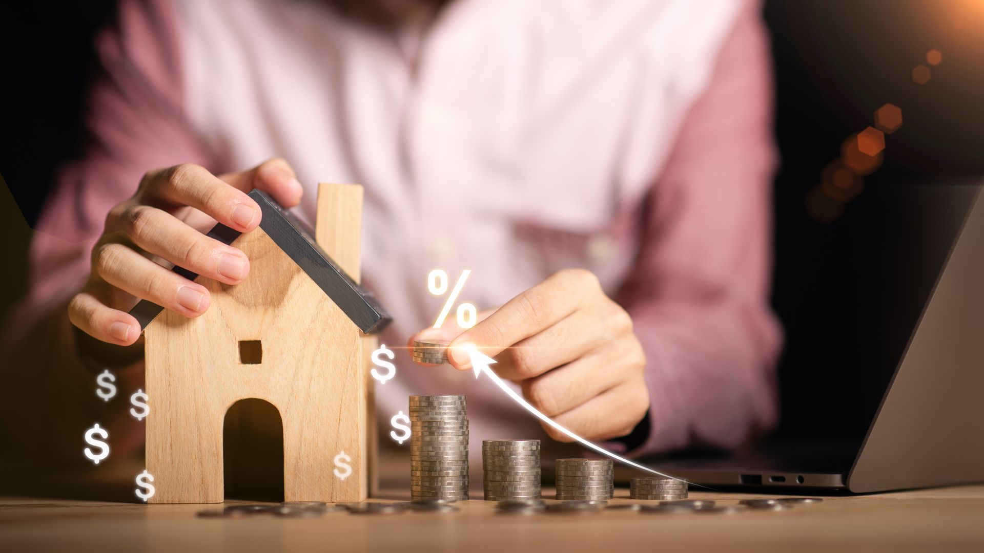 A person is sitting at a table holding a wooden house and coins.