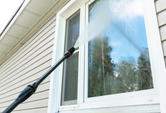 Extending window-washing pole cleaning a white house window beside beige siding