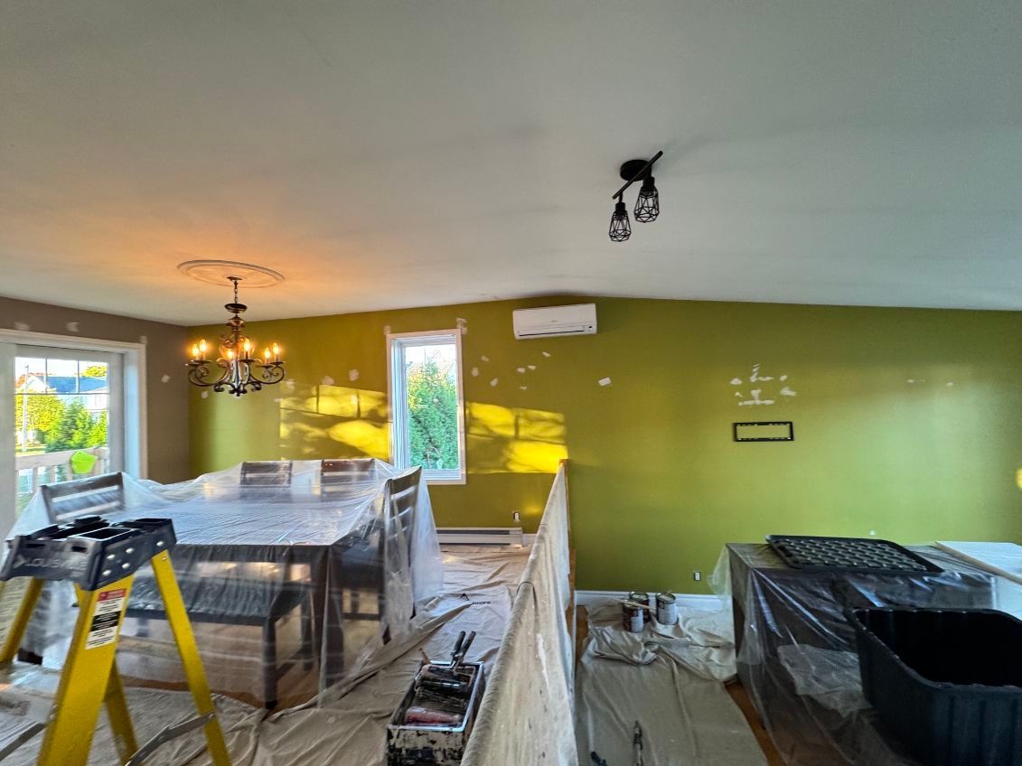 Pièce aux murs partiellement peints, en vert et beige, meubles recouverts pour être peints.