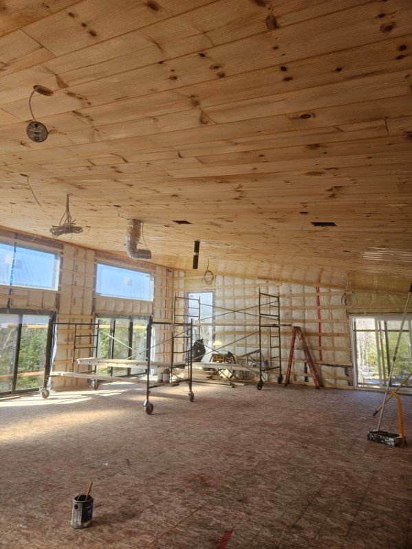 Intérieur d'un bâtiment inachevé avec plafond en bois, isolation, fenêtres et matériaux de construction.