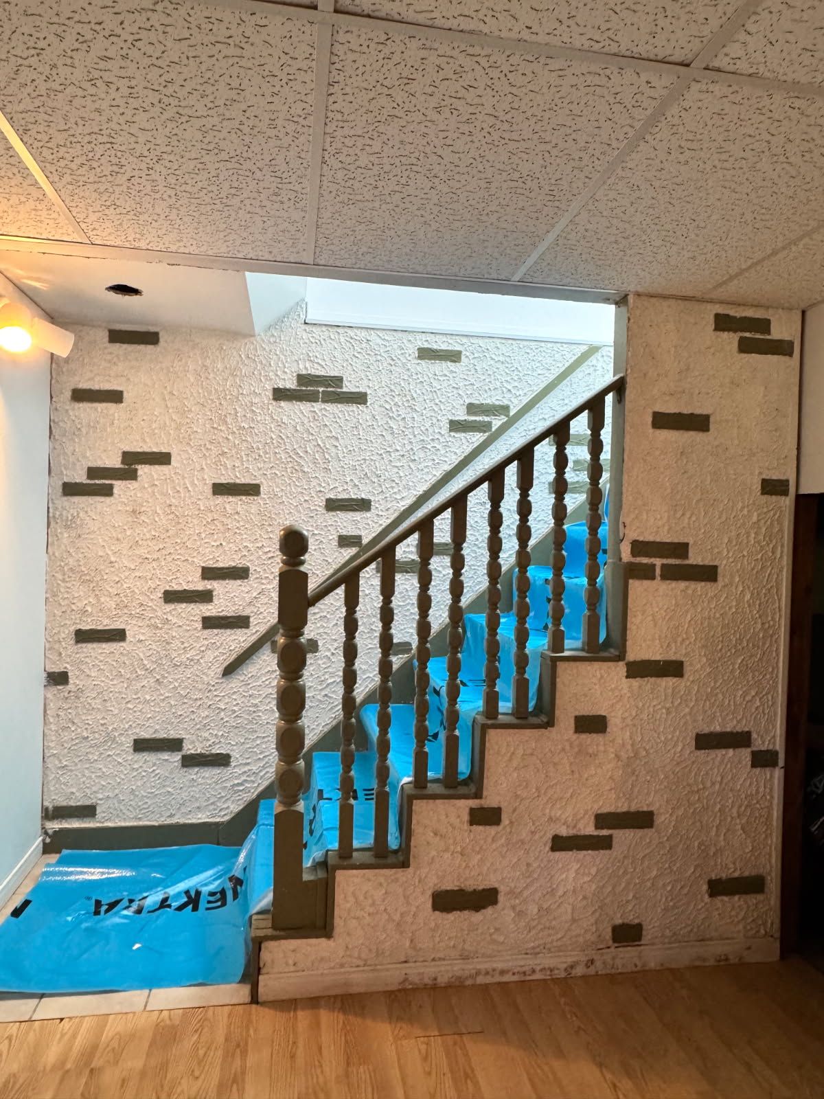 Escalier avec rampe en bois et muret en pierre décorative. Revêtement de protection bleu sur les marches.