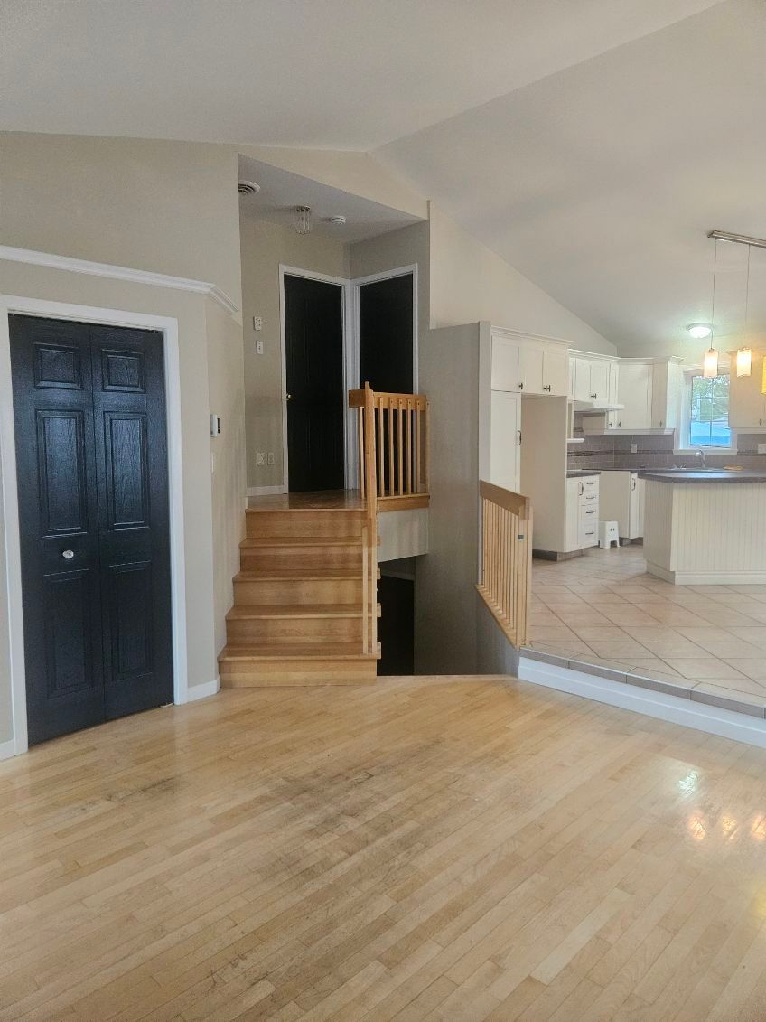 Vue intérieure : parquet, escalier, portes noires, placards blancs, murs beiges.