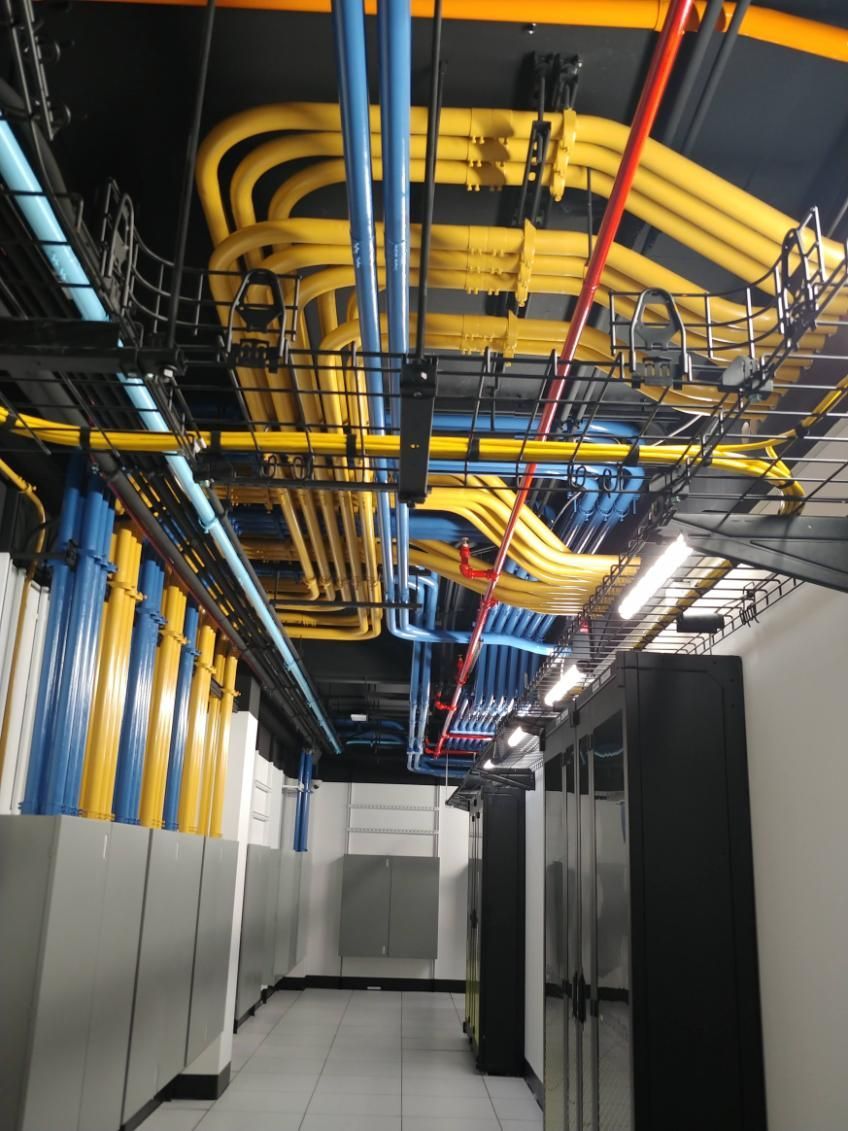 Plafond avec un réseau de tuyaux et de conduits colorés dans une salle serveur.