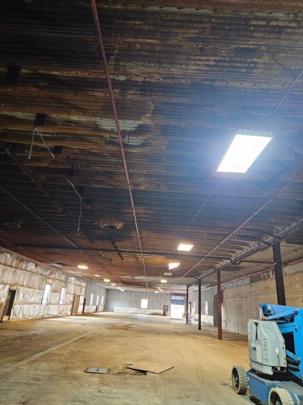 Vue intérieure d'un grand entrepôt avec un plafond endommagé, une verrière et un ascenseur.