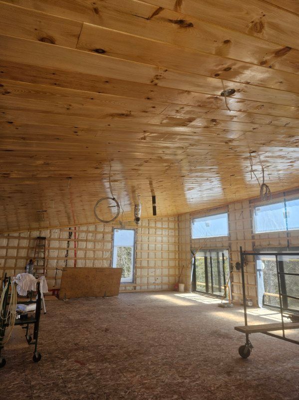 Intérieur d'un bâtiment avec plafond en bois, murs bruts et fenêtres. Présence d'échafaudages et de matériel.
