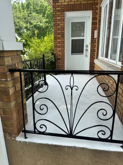 Rambarde en fer forgé noir sur un porche avec une porte blanche et une façade en briques.