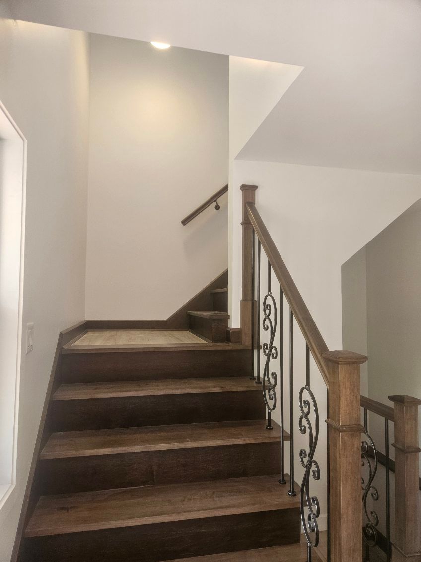 Escalier en bois avec marches brun foncé et parois claires. Rambarde décorative en fer forgé.