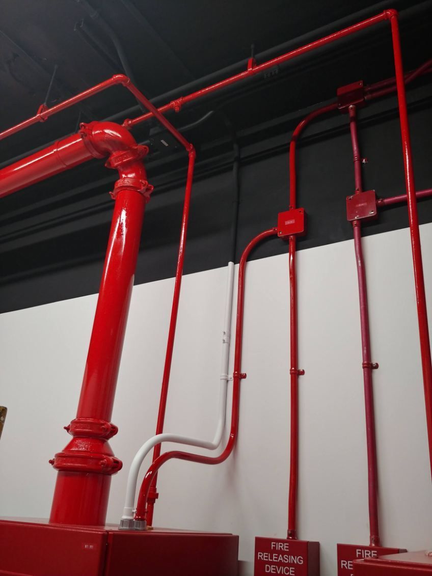 Tuyaux d'extincteurs automatiques rouges et conduits électriques fixés sur des murs blancs et noirs.