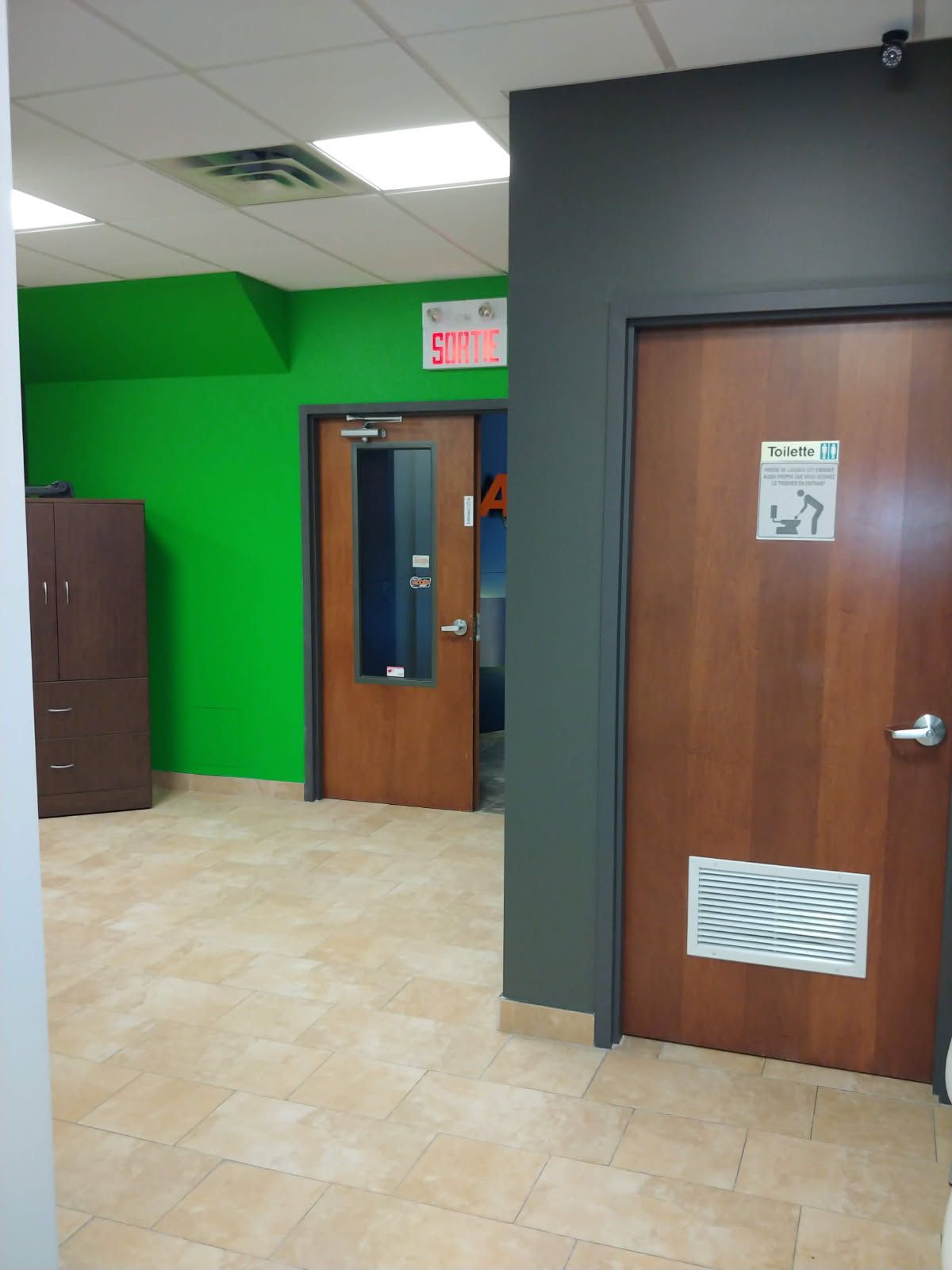 Couloir de bureau avec murs verts et gris, deux portes fermées, sol carrelé.