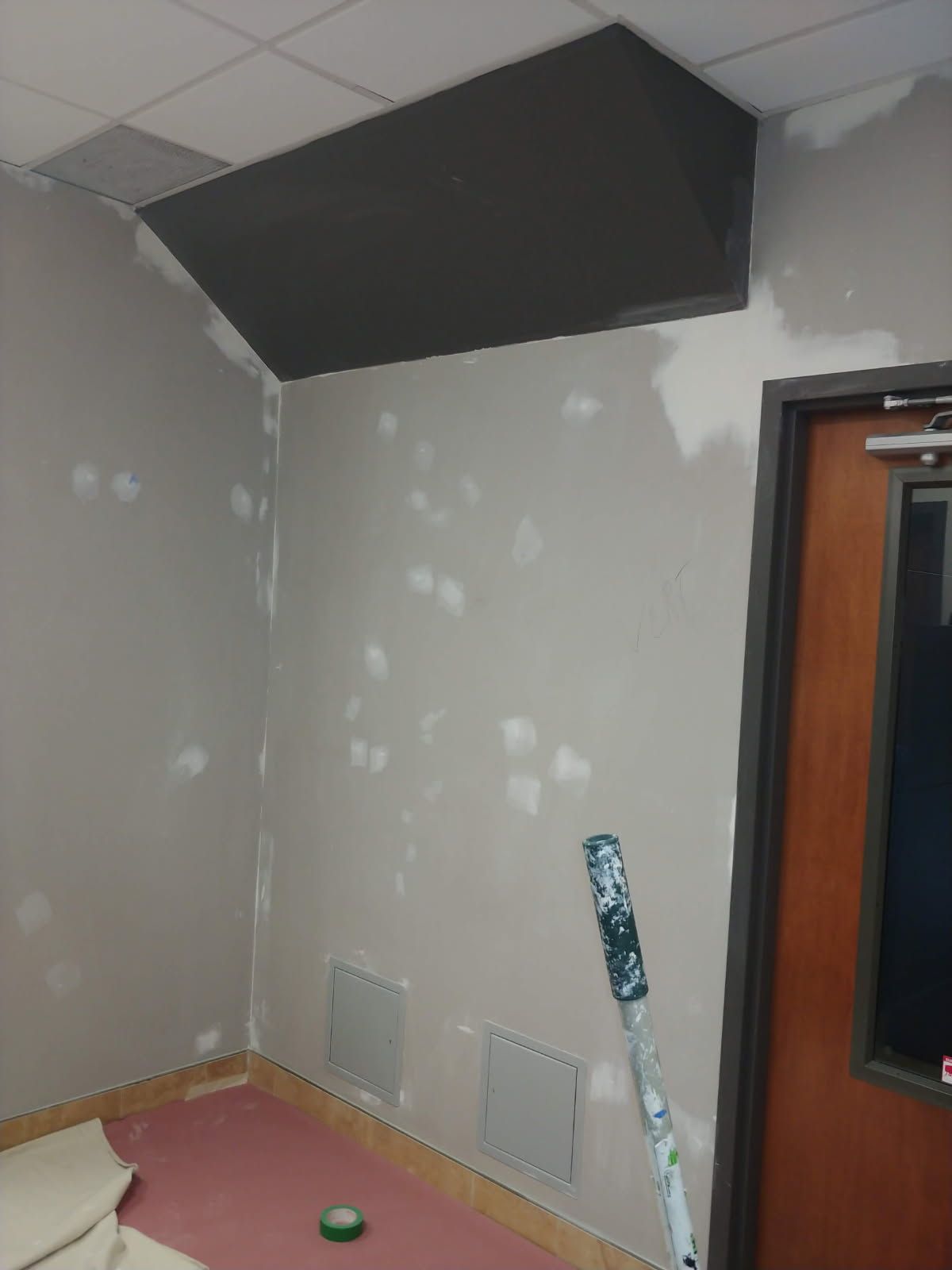 Pièce aux murs, au plafond et au panneau d'insonorisation gris. Rouleau à peinture sur le mur et l'encadrement de la porte.