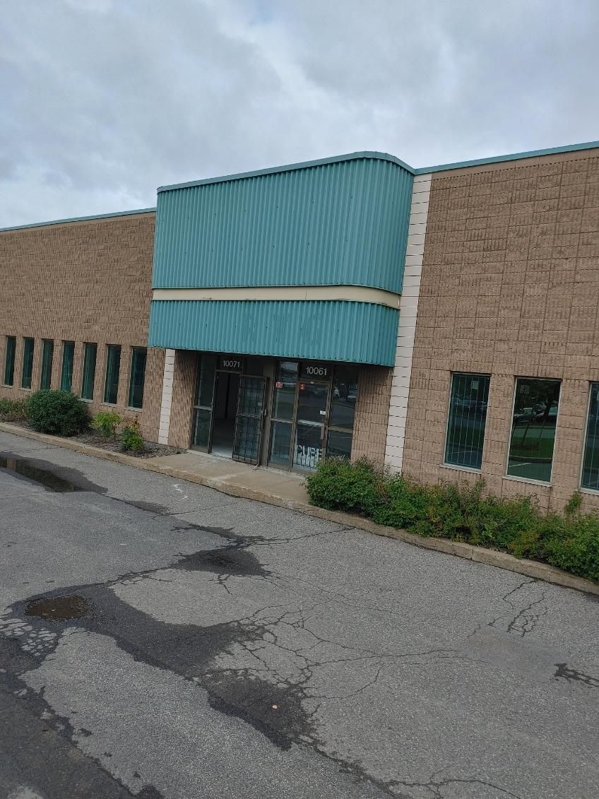 Un bâtiment en briques abandonné, avec un auvent turquoise et des portes sombres. Trottoir devant.