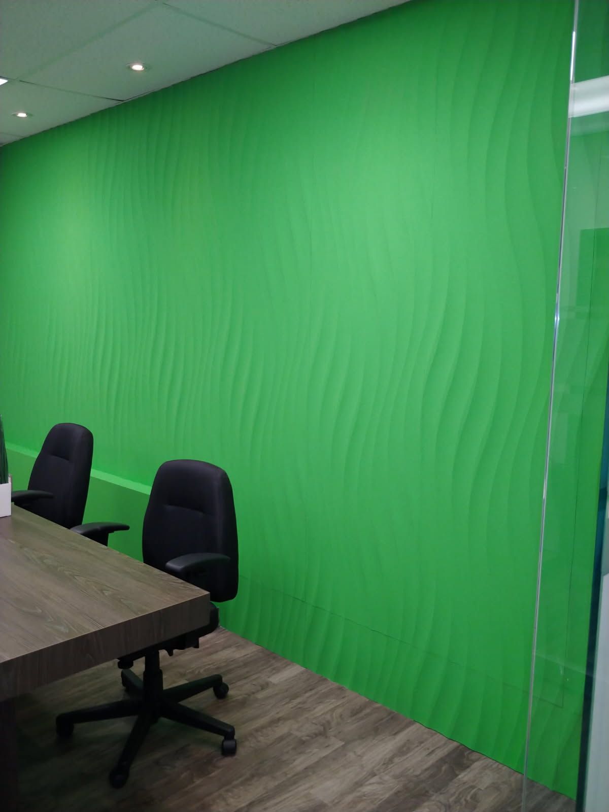 Mur texturé vert dans un bureau avec un bureau, des chaises et une cloison vitrée.