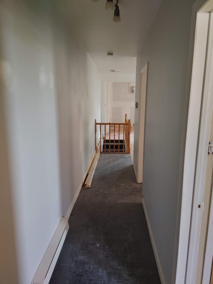 Couloir étroit aux murs gris et à la moquette, menant à un escalier en bois.