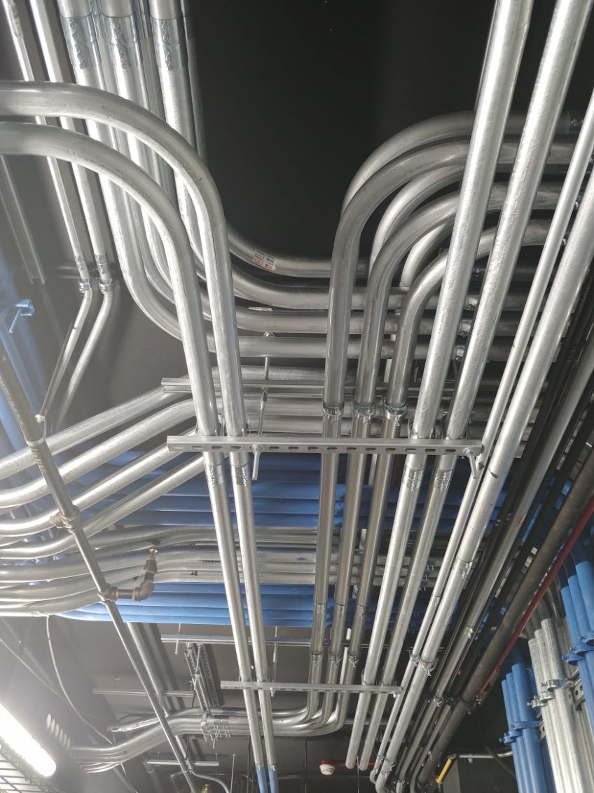 Vue de dessus de plusieurs conduits métalliques, probablement pour le câblage électrique, sur un plafond sombre.