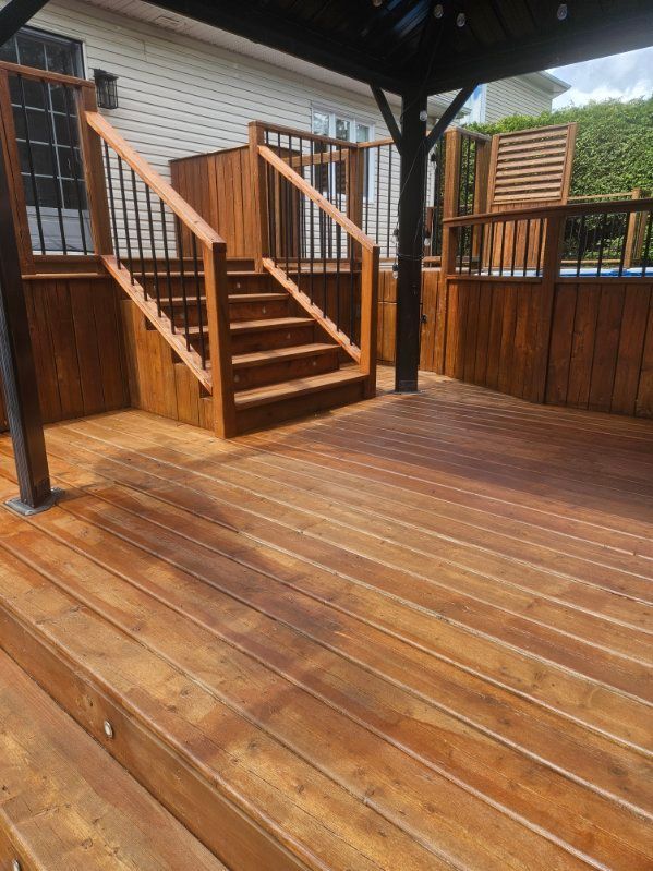 Terrasse en bois avec escalier, pergola et brise-vue. Le bois brun est humide et brillant.