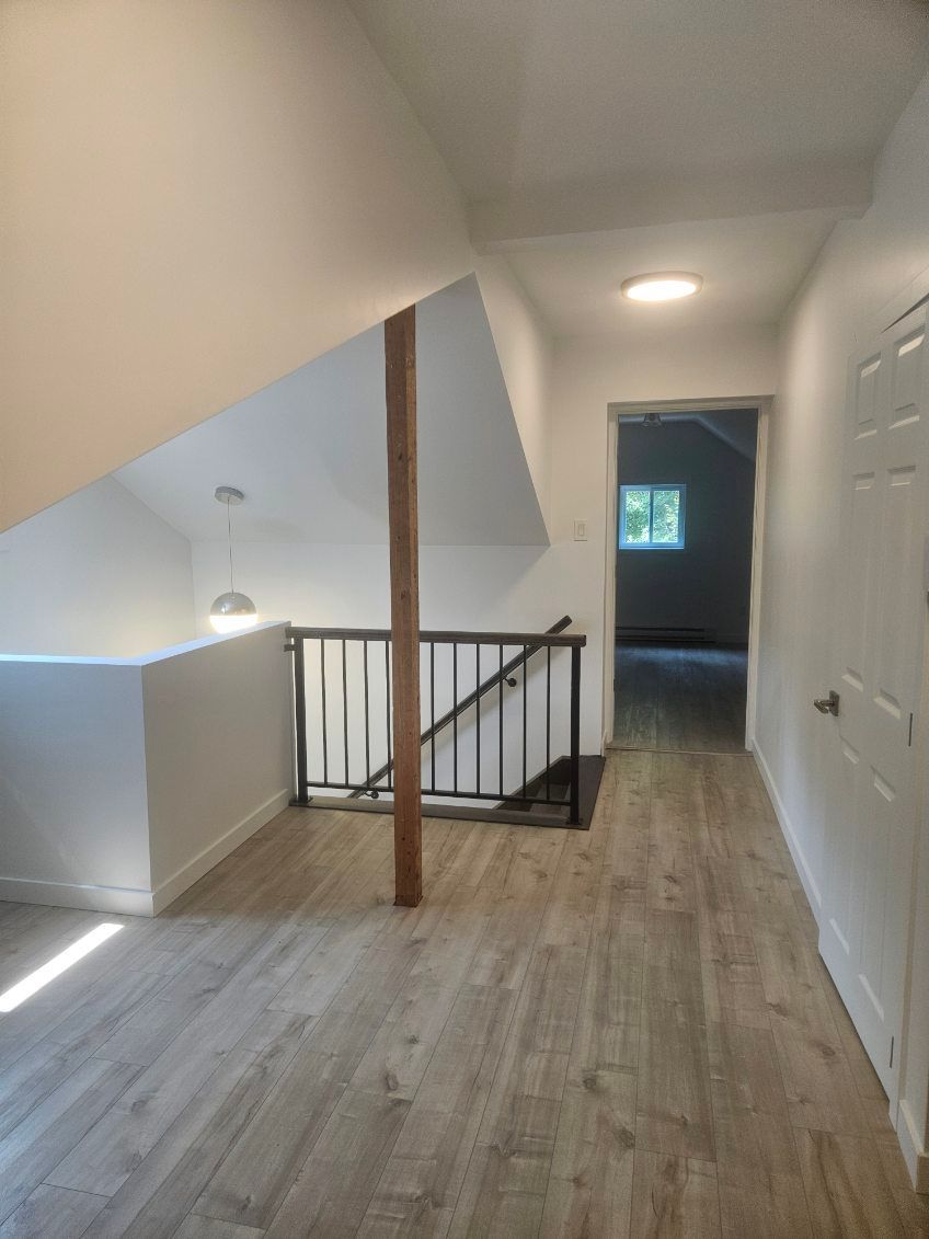 Couloir de mezzanine avec plafond mansardé, poutre de soutien en bois, rambarde, porte et parquet clair.
