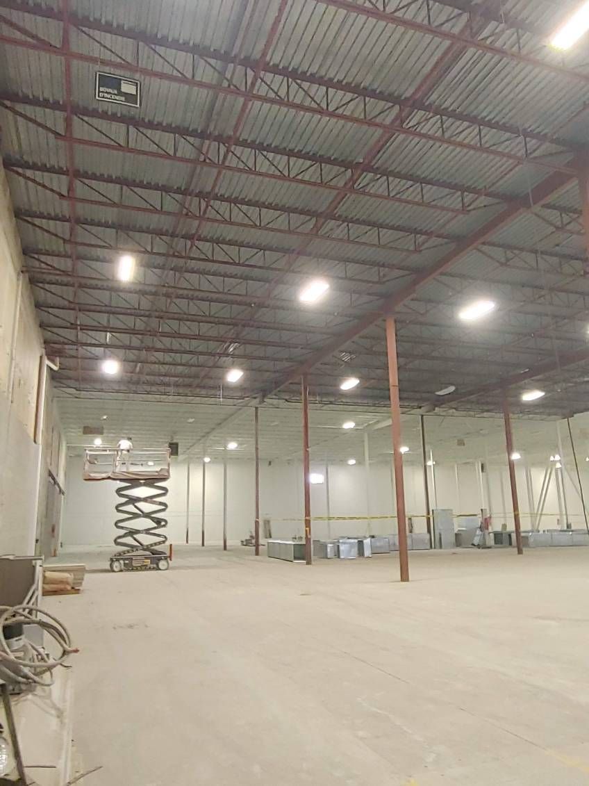 Intérieur d'un grand entrepôt avec un haut plafond, des poutres métalliques et un éclairage zénithal.