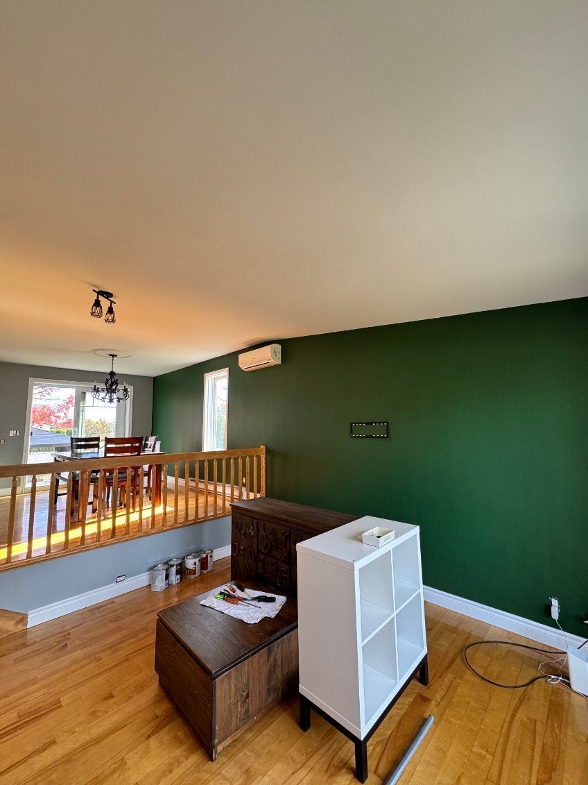 Salon avec parquet, murs gris et verts et un escalier en bois.