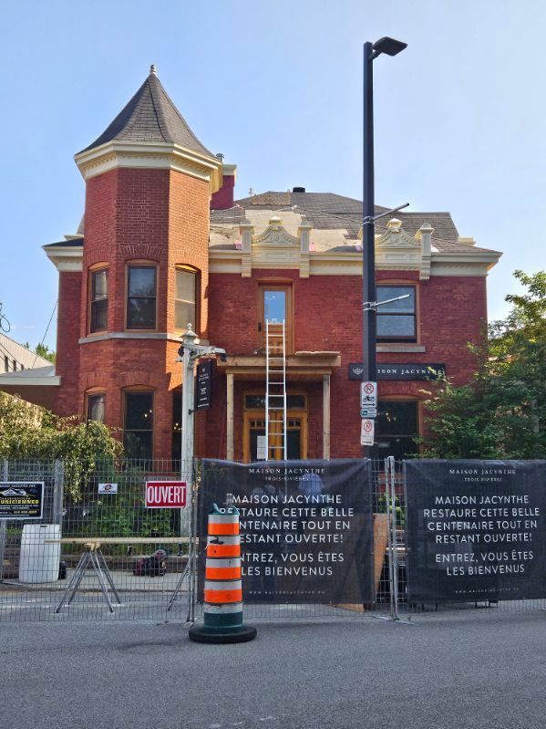 Bâtiment en briques rouges avec une tour, travaux en cours, barricades, panneaux.