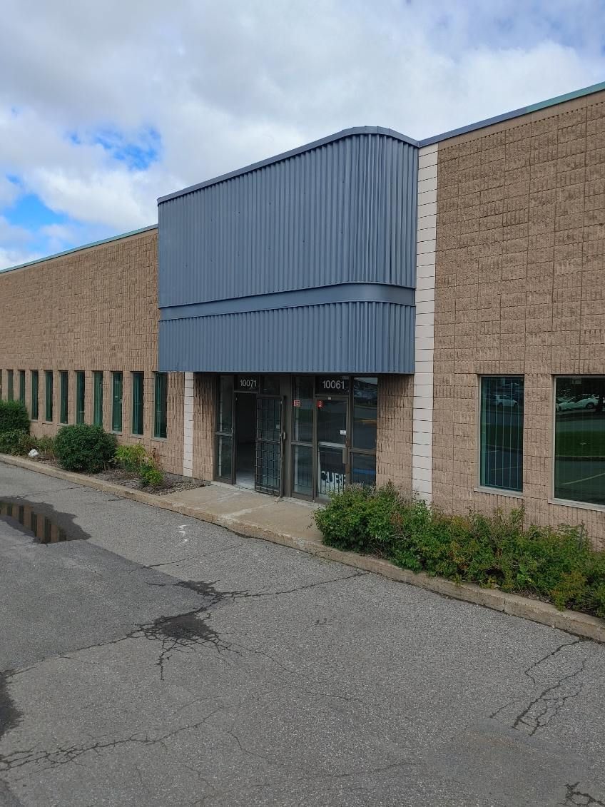 Extérieur d'un bâtiment industriel en briques avec un auvent métallique bleu au-dessus de l'entrée. Asphalte au premier plan.