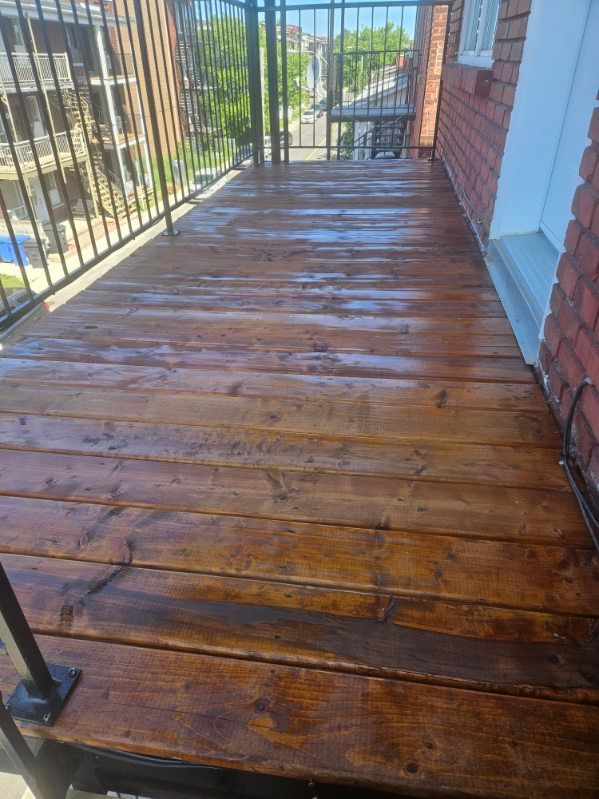 Terrasse en bois, teintée en brun, avec rambarde et muret en briques. Humide après nettoyage.