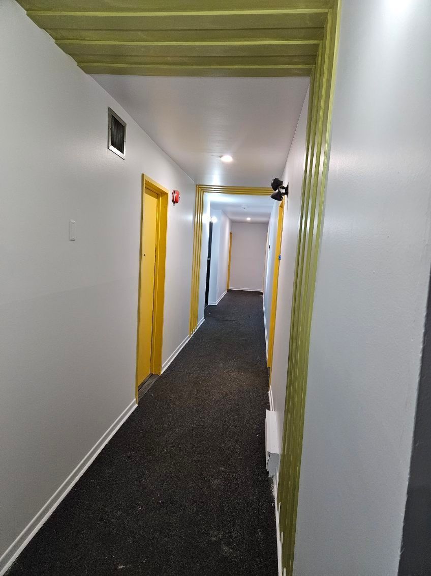 Long couloir aux murs gris, portes dorées et moquette foncée.